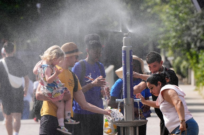 People refresh at a public water distribution in the center of Paris, France, during the opening ceremony of the 2024 Summer Olympics, Tuesday, July 30, 2024. Temperatures went up to 34 degrees Celsius. (AP Photo/Martin Meissner)