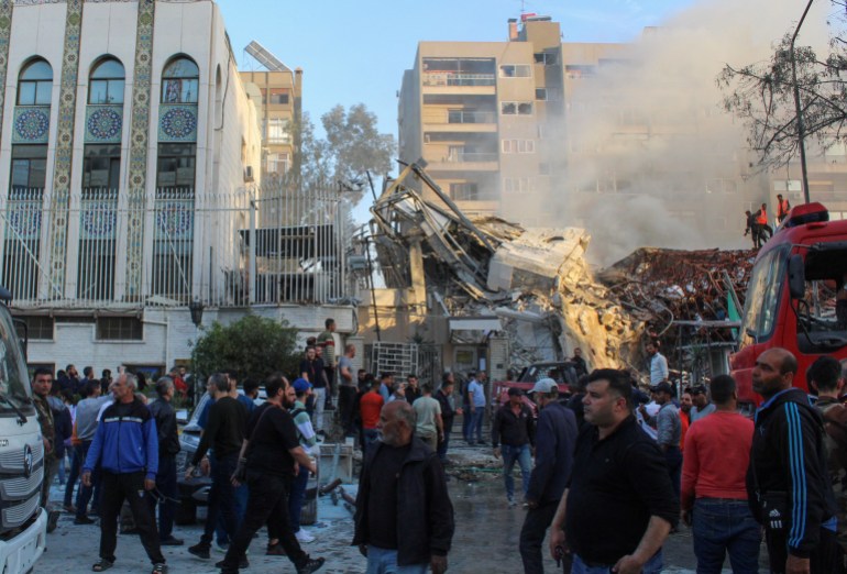 Members of the civil defence stand near a damaged site after what Syrian and Iranian media described as an Israeli air strike on Iran's consulate in the Syrian capital Damascus