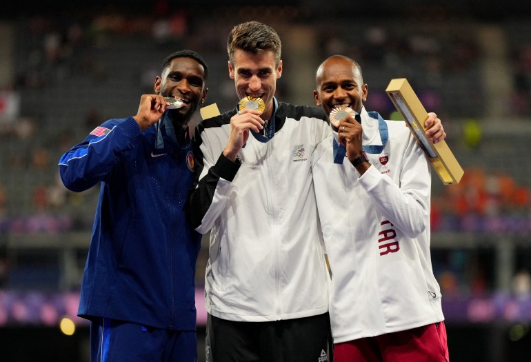 Paris 2024 Olympics - Athletics - Men's High Jump Victory Ceremony - Stade de France, Saint-Denis, France - August 10, 2024. Gold medallist Hamish Kerr of New Zealand celebrates on the podium with silver medallist Shelby McEwen of United States and bronze medallist Mutaz Essa Barshim of Qatar REUTERS/Aleksandra Szmigiel