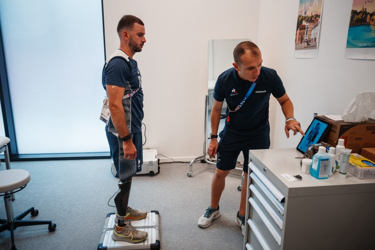 French para-athlete Alexis Sanchez (L) chats with a technician at the Ottobock prosthetic repair centre in the Paralympic athletes' village in Saint-Denis on August 24, 2024, ahead of the Paris 2024 Paralympic Games. - The centre provides free adjustments and repairs of prosthetics, orthotics, and equipment for athletes and attendees during the Paris 2024 Paralympic Games. (Photo by Dimitar DILKOFF / AFP)